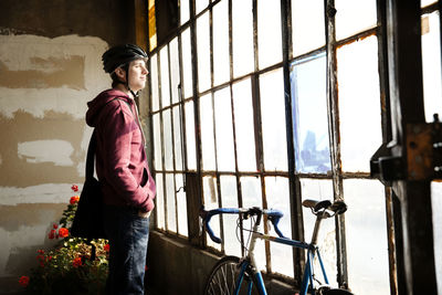 Man with hand in pocket looking away while standing by window