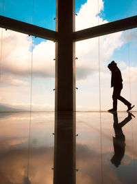 Silhouette man standing by window against sky