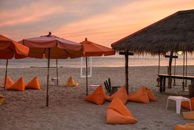Beanbag chairs and parasols on beach against sky during sunset