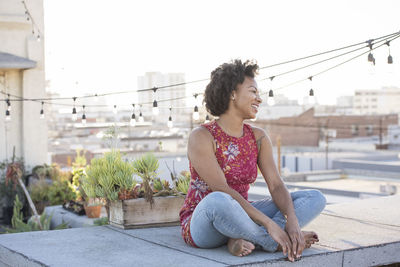 Young woman sitting on rooftop terrace, enjoying the sun