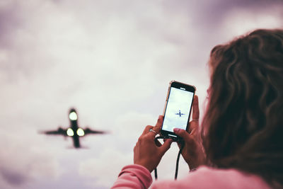 Woman photographing airplane in sky with mobile phone