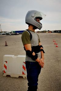 Side view of boy with helmet standing on land against sky