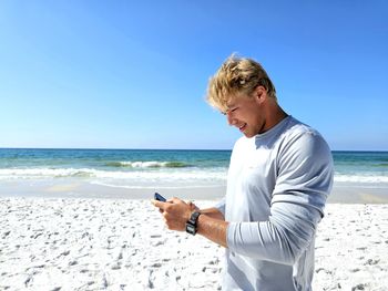 Happy millennial guy texting a friend on the beach.