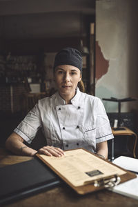 Portrait of chef with menu sitting at restaurant