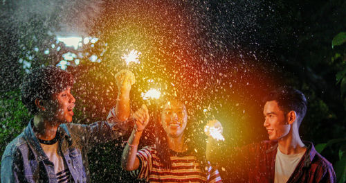 Happy friends holding sparklers at night