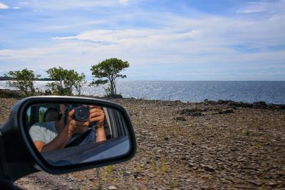 Reflection of man photographing with woman in side-view mirror of car