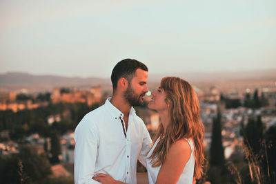 Happy romantic couple kissing against city during sunset