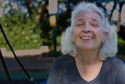 Portrait of a smiling gray-haired lady in the park on a swing. copy space.