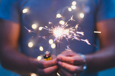 Midsection of person holding illuminated sparkler at night