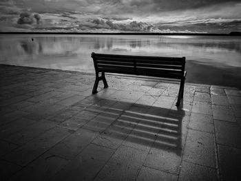 Empty bench by lake against sky