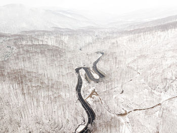 Curvy windy road in snow covered forest, top down aerial view.