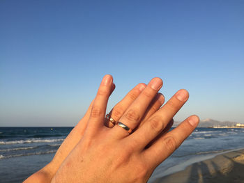 Close-up of hand against sea against clear sky