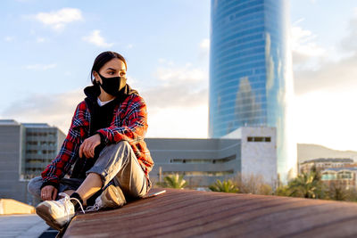 Portrait of young woman sitting against sky in city