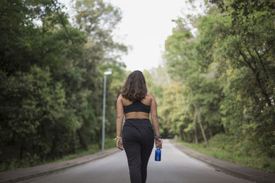 Rear view of woman standing on road amidst trees