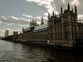 Buildings by river against cloudy sky