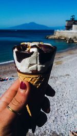 Cropped image of hand holding ice cream cone at beach