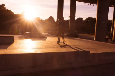 Silhouette man skateboarding on street against sky during sunset