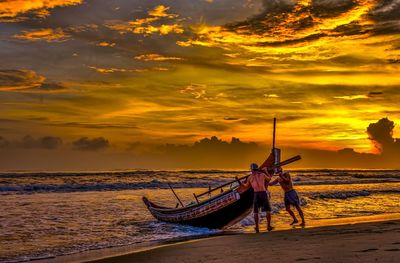 Fishermen pushing boat in sea against sky during sunset
