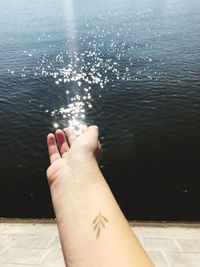 Cropped hand against lake with sunlight reflection