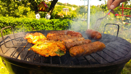 Cropped hand cooking meat on barbecue grill in yard