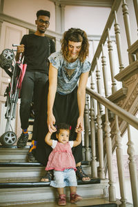 Mother holding hands of daughter moving down on steps in apartment