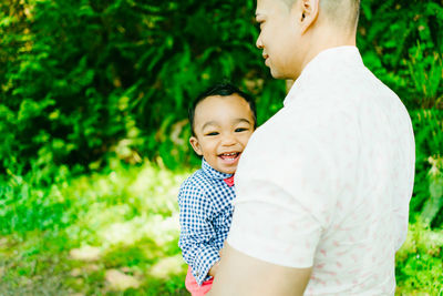 View from behind of a father carrying his smiling baby boy