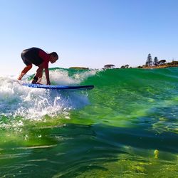 Full length of boy surfing in sea against sky
