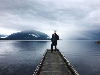 Man standing on pier over lake against sky