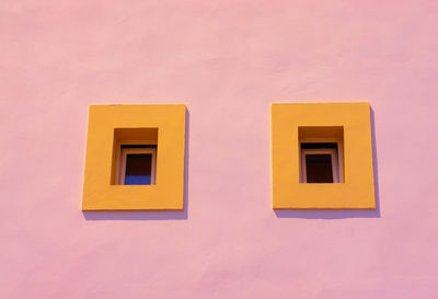 Low angle view of yellow windows in pink wall