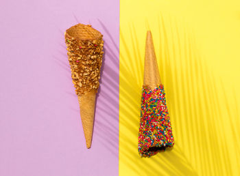 Colorful ice cream waffle cones and palm leaf shadow on pastel purple and yellow background. flat la