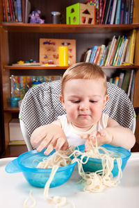 Cute baby boy with pasta bowls on table sitting at home