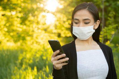 Young woman using phone while standing on plants
