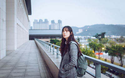 Portrait of young woman standing against railing in city