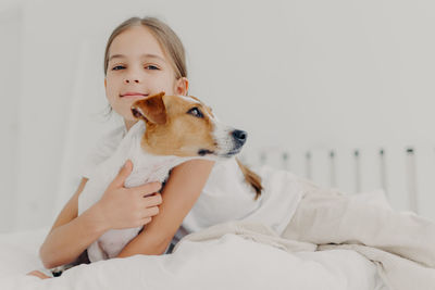 Portrait of girl with dog sitting on bed at home