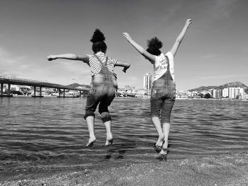 Rear view of sisters jumping at beach