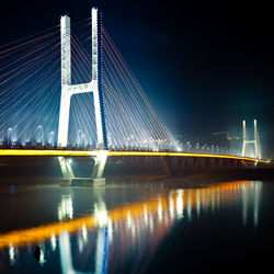 Illuminated bridge over river against sky at night