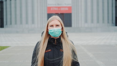 Portrait of young woman standing against wall in city