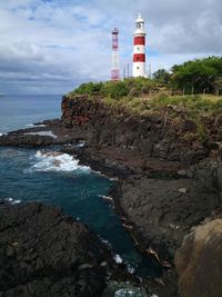 Lighthouse by sea and buildings against sky