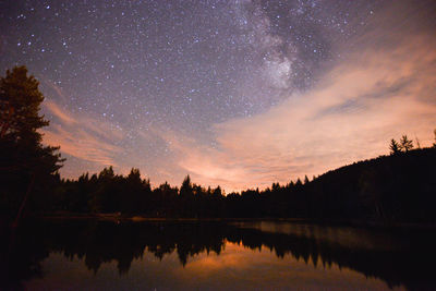 Reflection of silhouette trees in lake against sky at night