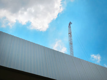 Low angle view of crane by building against sky