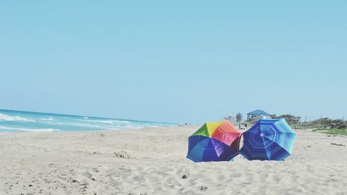 Umbrellas on sandy beach against clear blue sky