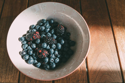 High angle view of berry fruits in bowl on wooden table