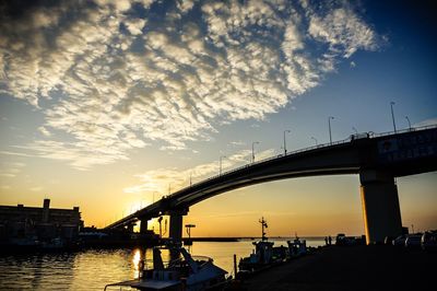 Low angle view of bridge over river against cloudy sky during sunset