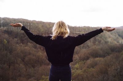 Rear view of woman with arms outstretched standing against sky