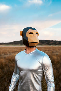 Anonymous person in geometric monkey mask looking away in yellow field on blurred background