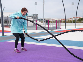 Full length of woman exercising with batter rope