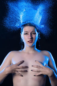 Portrait of naked young fashion model with splashing water against blue background