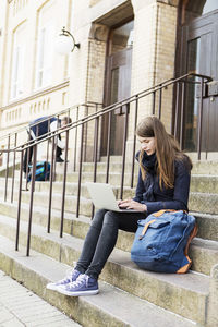 Young woman using laptop on steps of high school