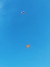 Low angle view of kites flying against clear blue sky