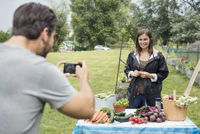 Mid adult man photographing woman standing at table full of garden vegetables